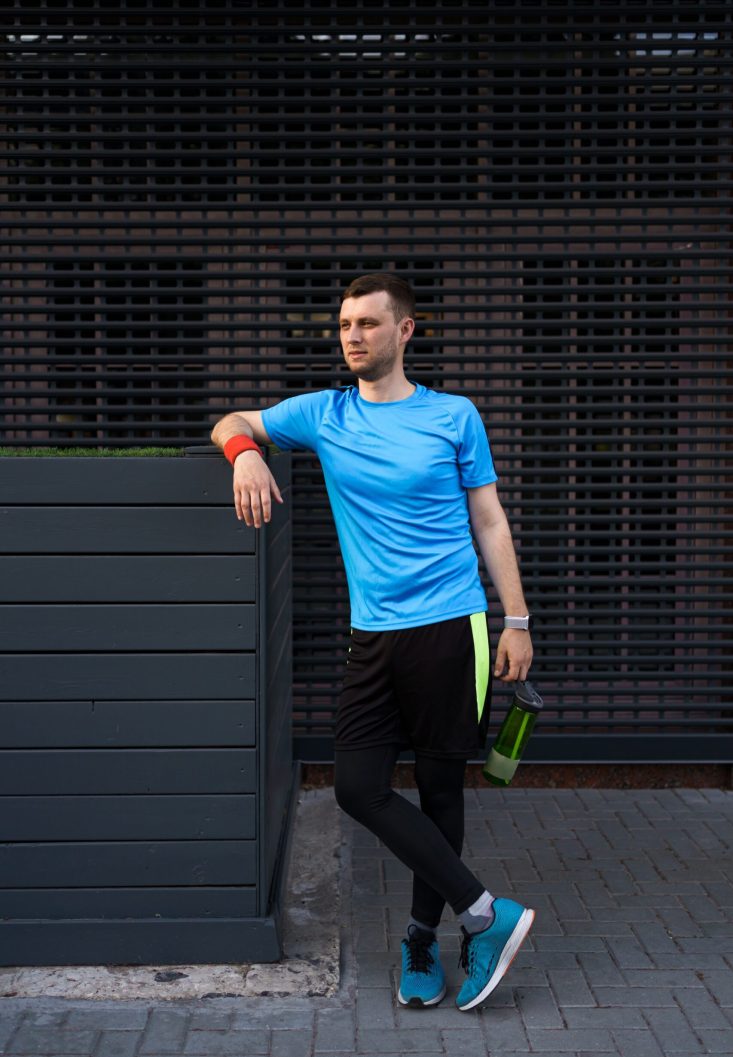 Portrait sporty man on gray urban background. Portrait city runner on a break concentraiting for a long marathon.